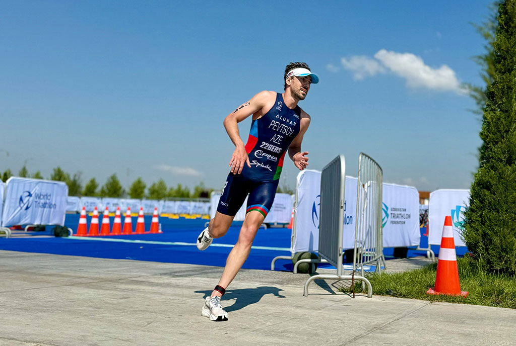 Image of triathletes running on a paved course with race numbers, focused expressions, and spectators visible along the route.