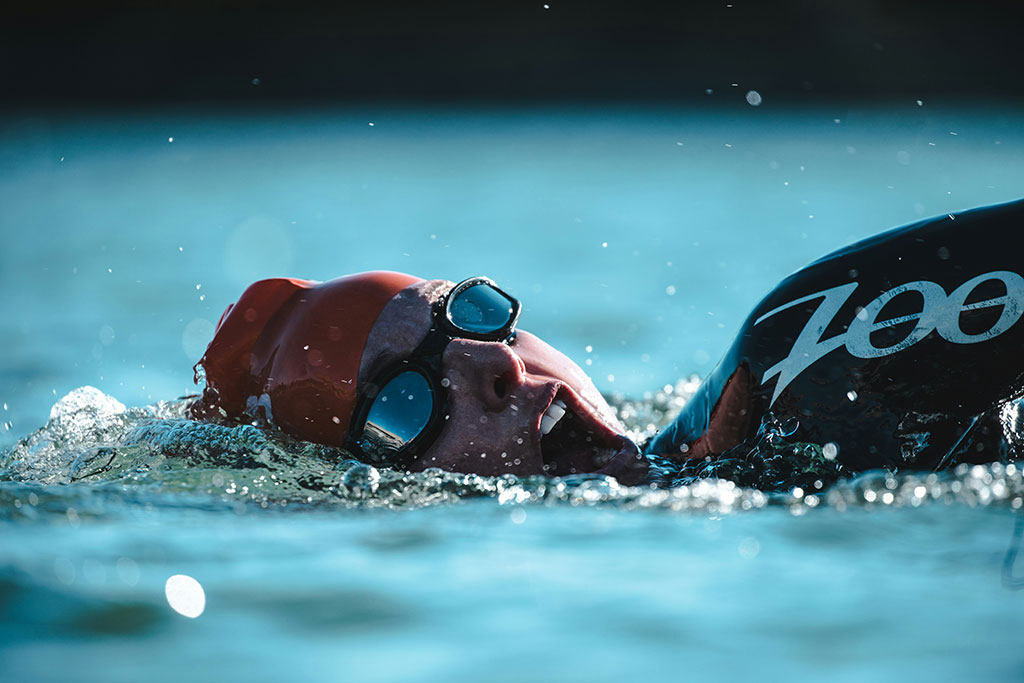 Image of triathlon swimmer in open water with goggles, taking a breath.