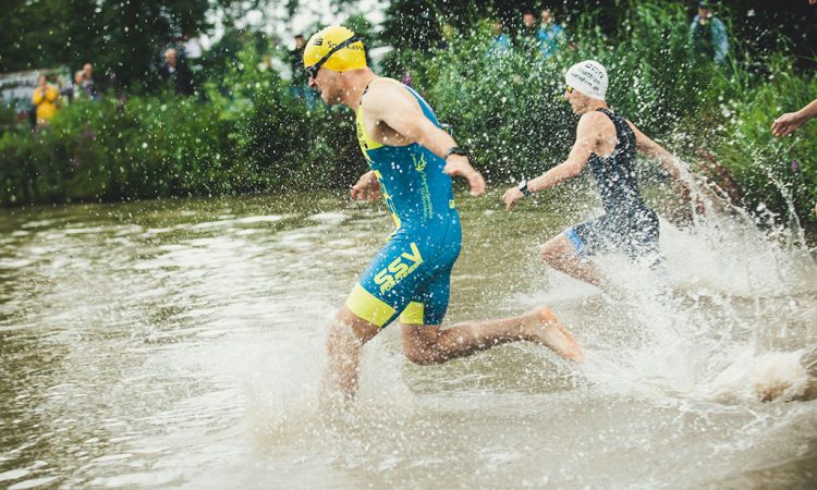 Image of triathletes in wetsuits swimming closely together in open water during the triathlon’s swim segment.
