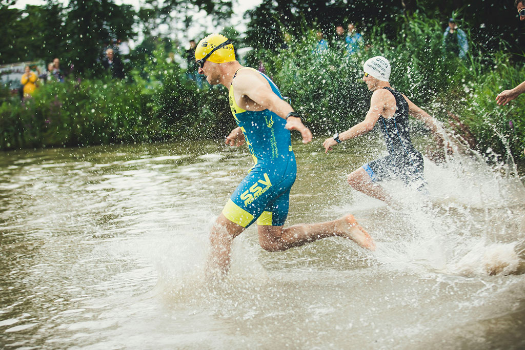 Image of triathletes in wetsuits swimming closely together in open water during the triathlon’s swim segment.
