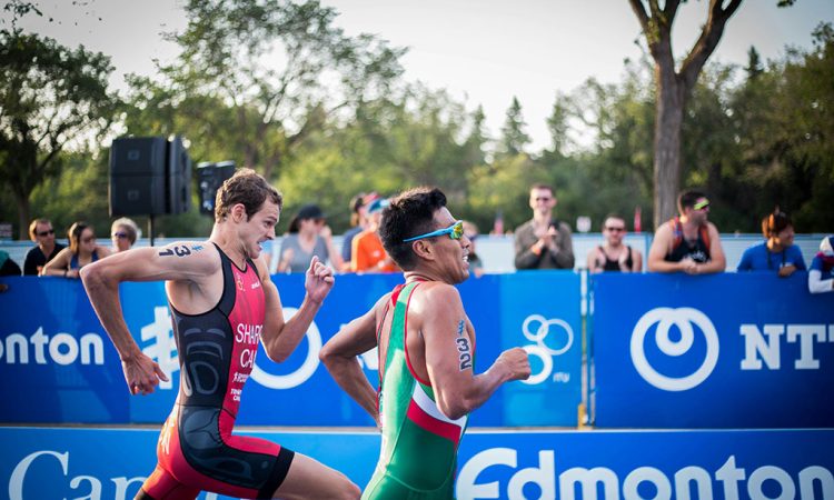 Image of two triathletes sprinting side by side toward the finish line as spectators cheer behind them.