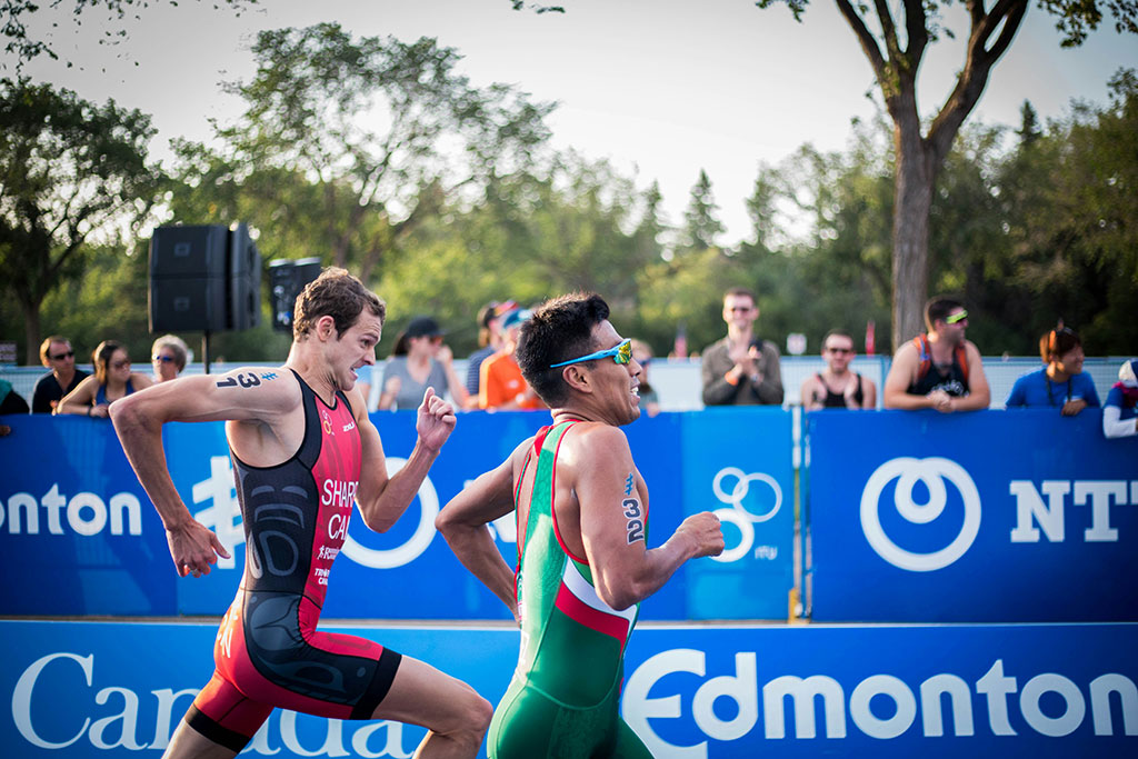 Image of two triathletes sprinting side by side toward the finish line as spectators cheer behind them.