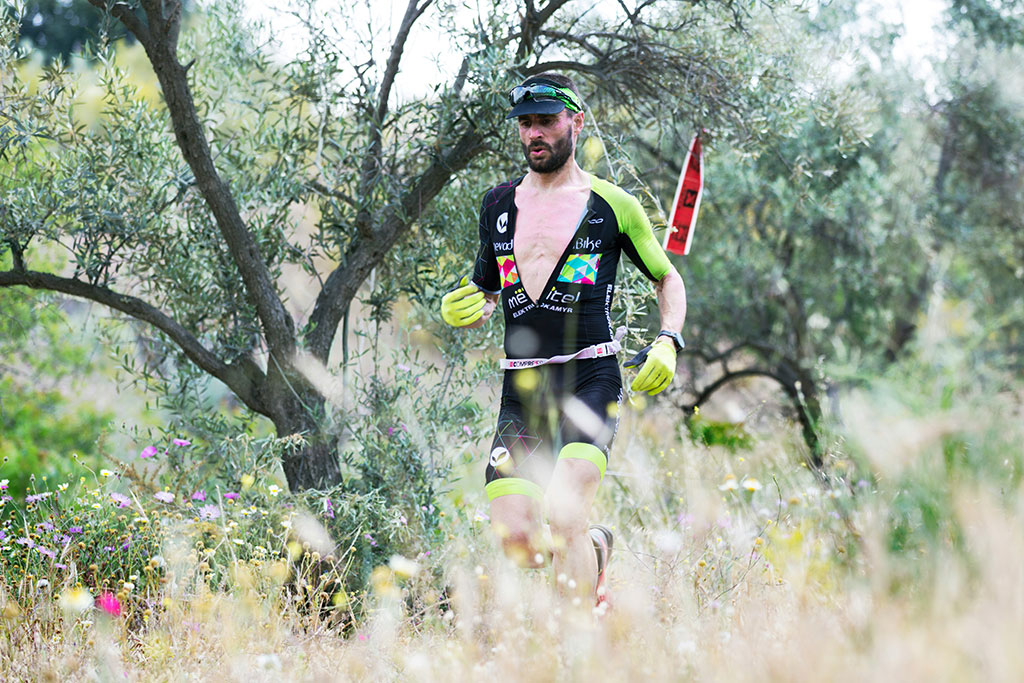 Image of a trail runner moving through tall grass and trees on a sunny day with a focused, determined expression.
